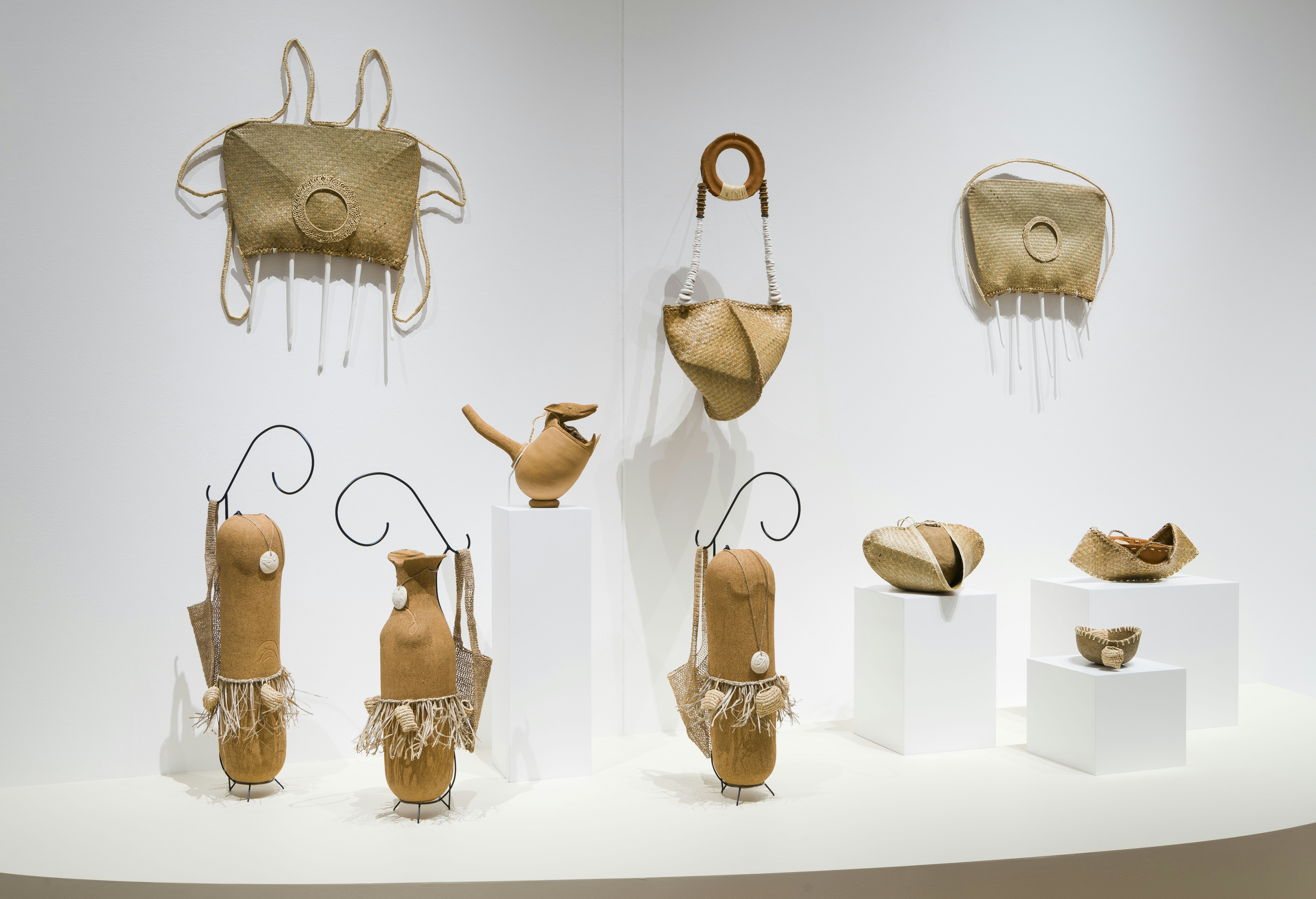 A series of bags woven from twine, fibre and raffia, installed above some sculptural vessels made from fired terracotta.