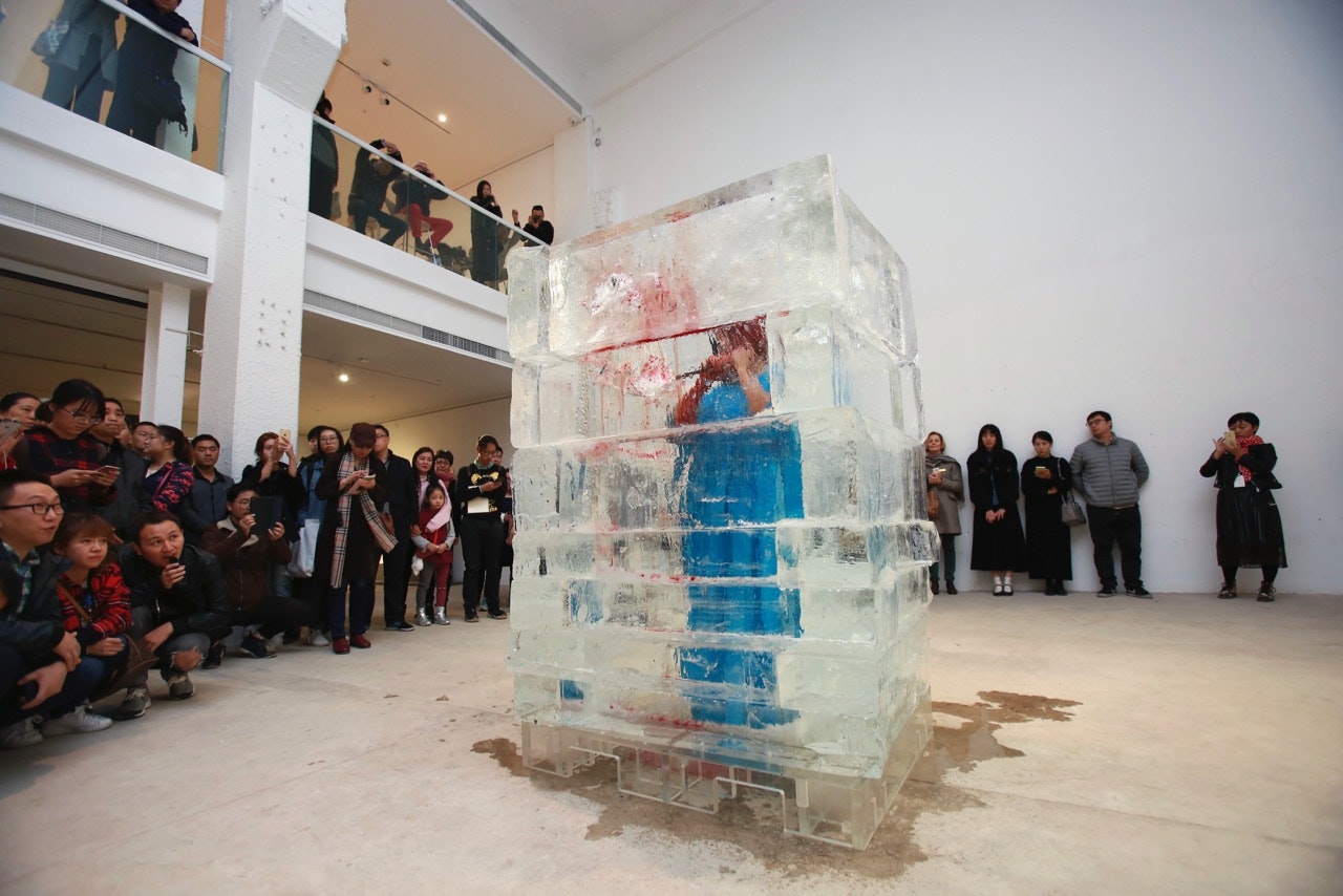 A huge block of ice, with a woman in a long, shapeless blue dress cutting into it from the other side. Part of the ice block is stained red with blood and running to the floor.