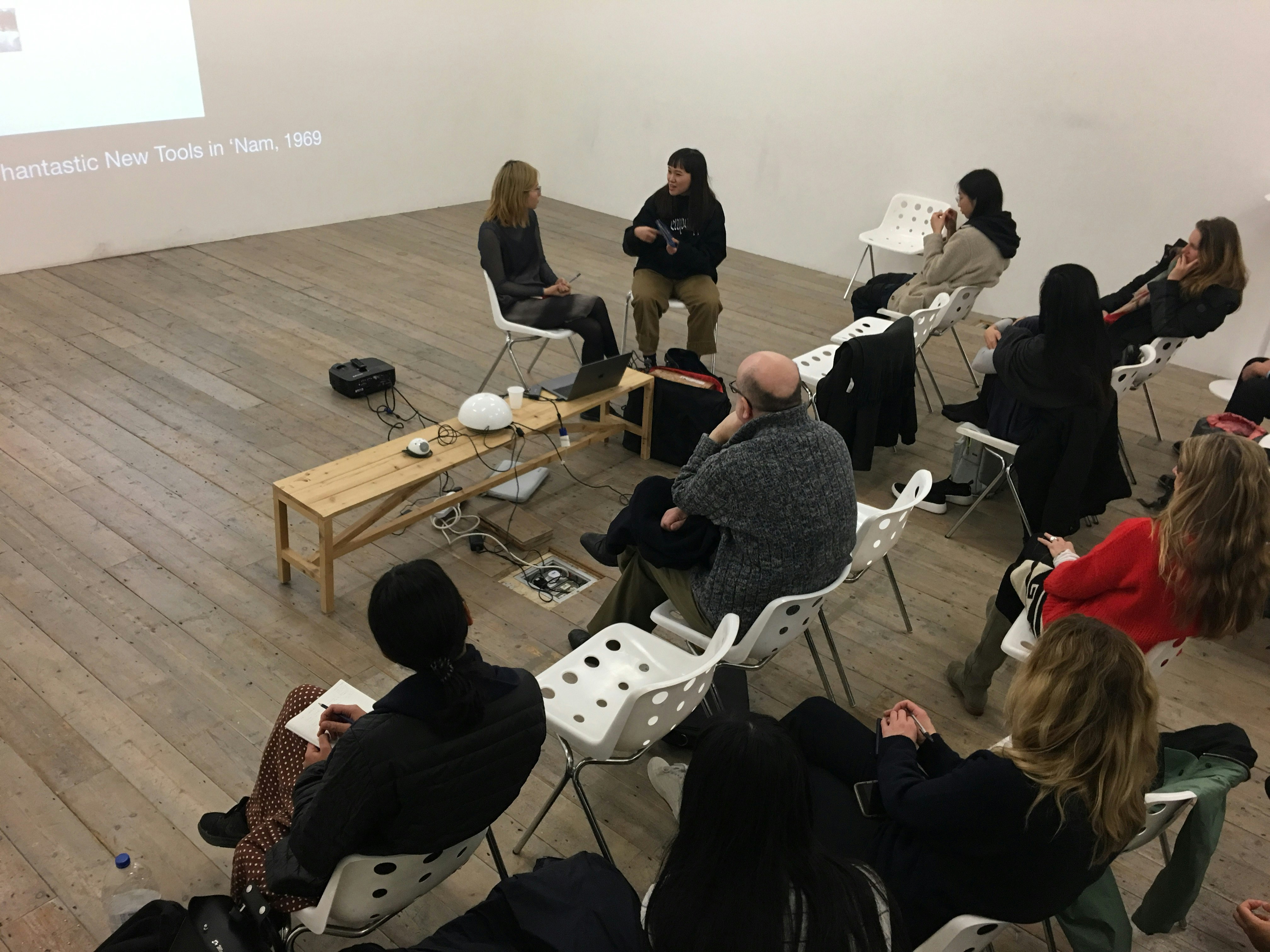 A group of seated patrons in a gallery listening to a conversation between two artists.