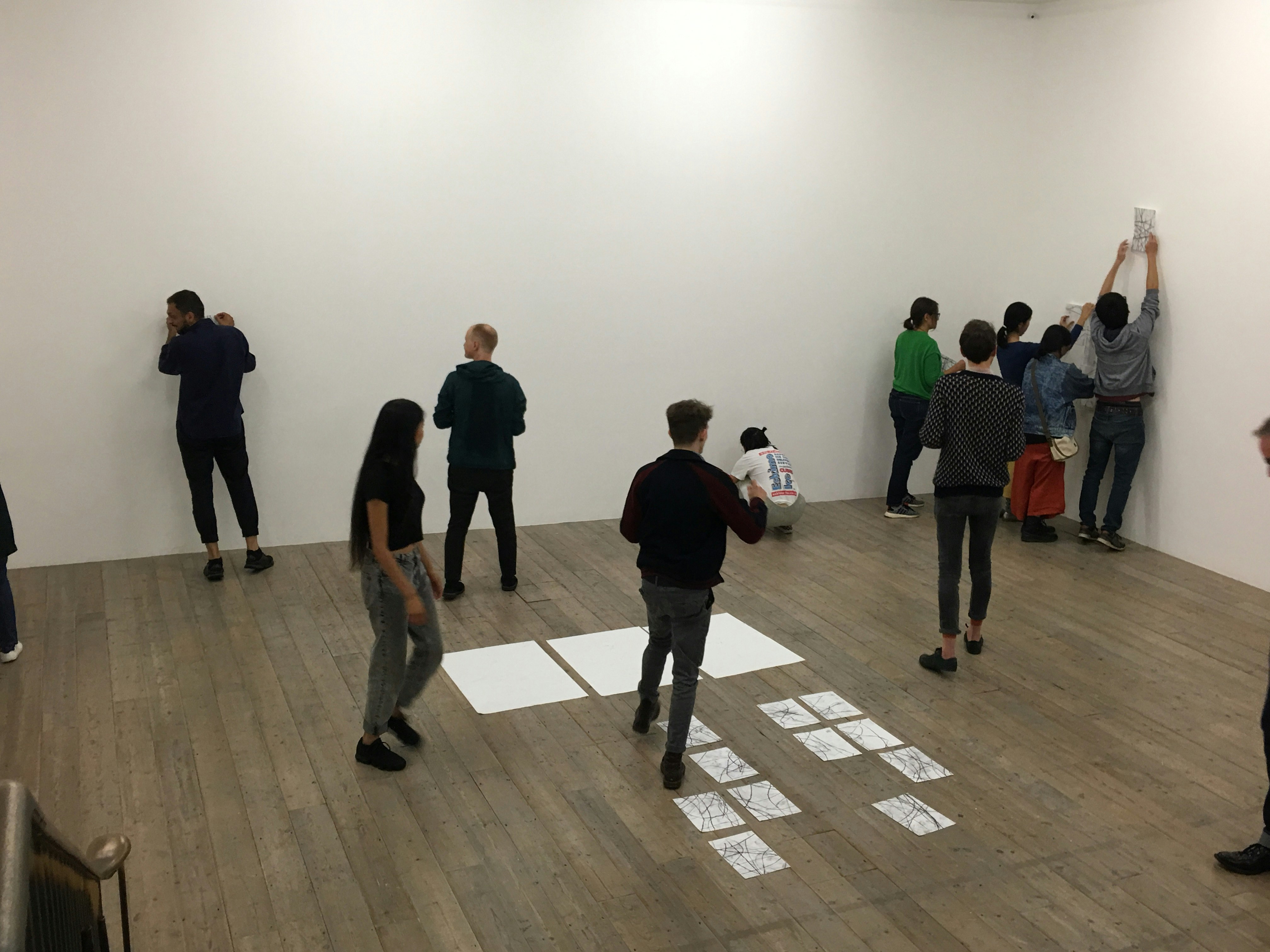 A group of gallery patrons placing A4 pieces of paper on the walls.