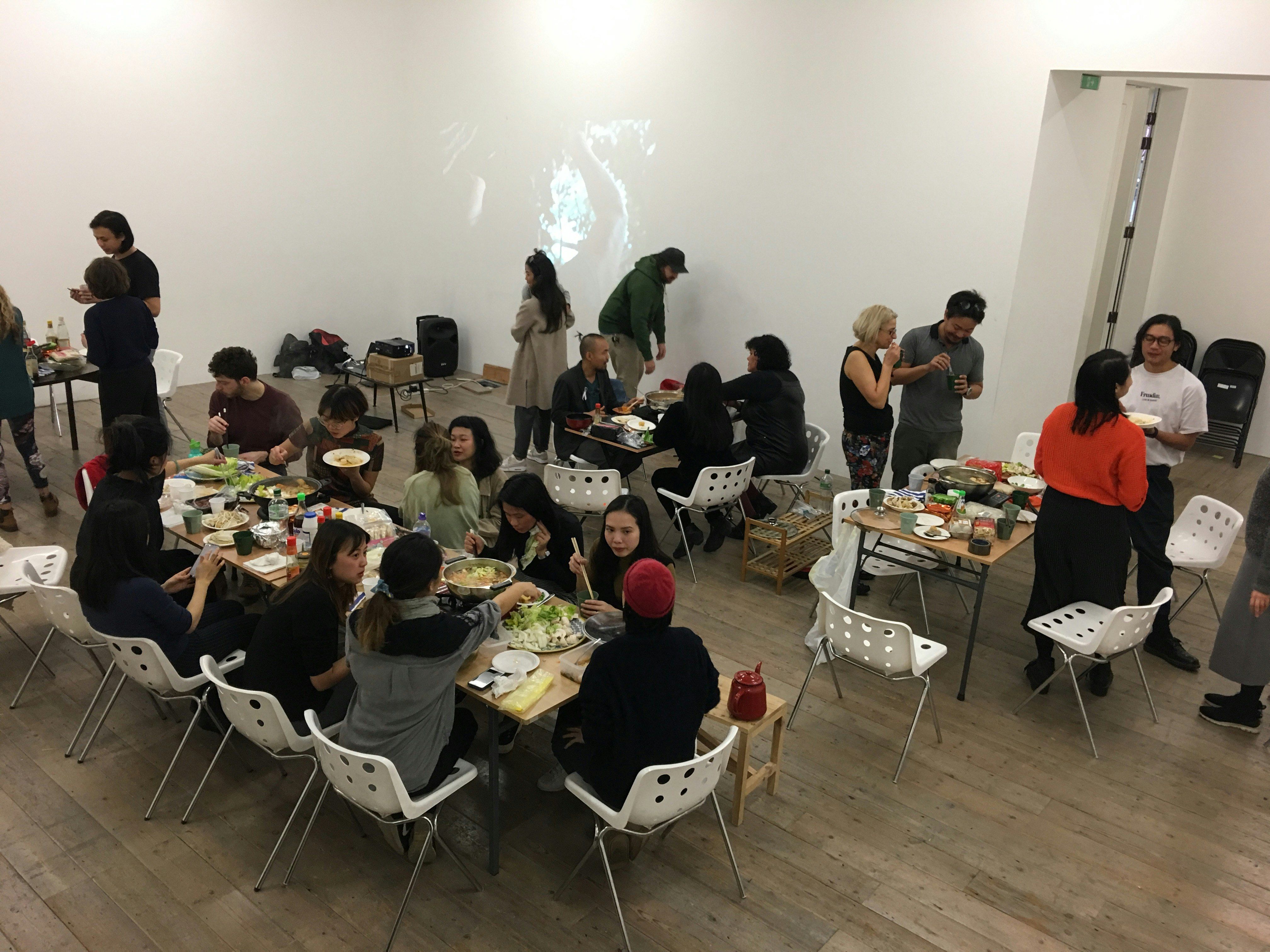A gallery set up as a dining space, with one long dining table serving hotpot and surrounding smaller tables where patrons eat together.