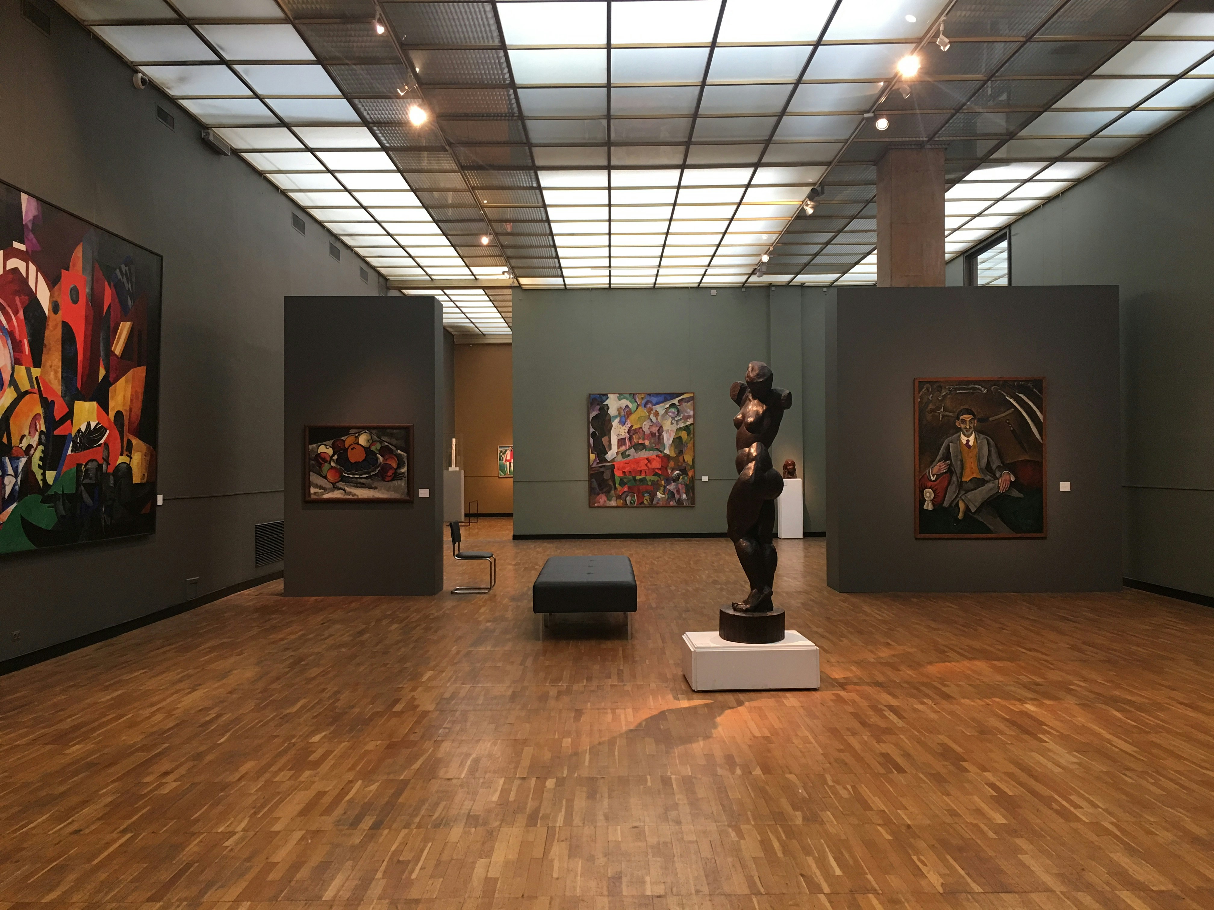 A bronze sculpture inside a gallery space, surrounded by geometrically striking Russian paintings.
