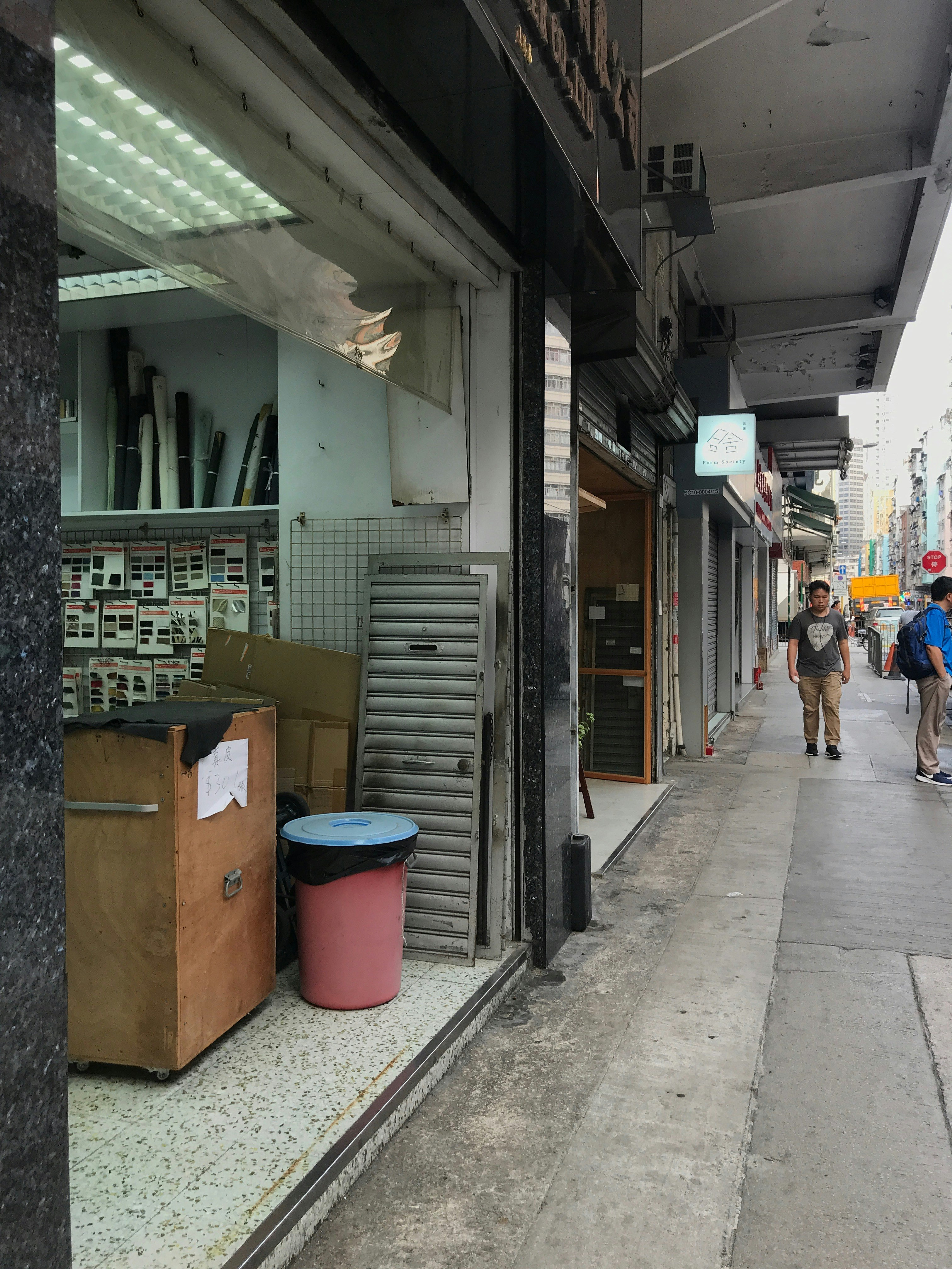 A street front of an open fabric store in Hong Kong, with some figures walking by on the street.
