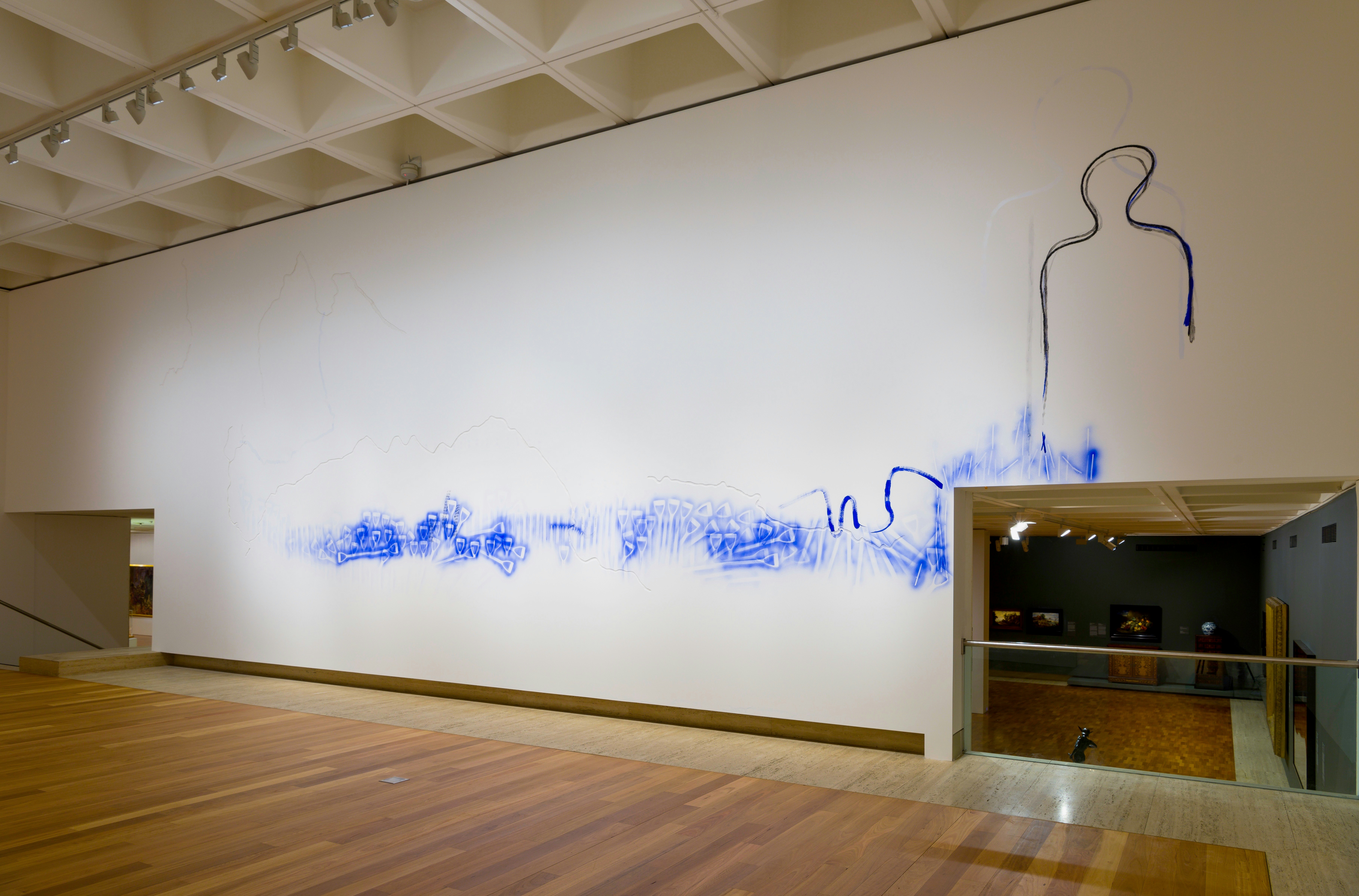 A high-ceilinged white wall in an art gallery painted with a blue substance under a painted outline that resembles a person's shadow.