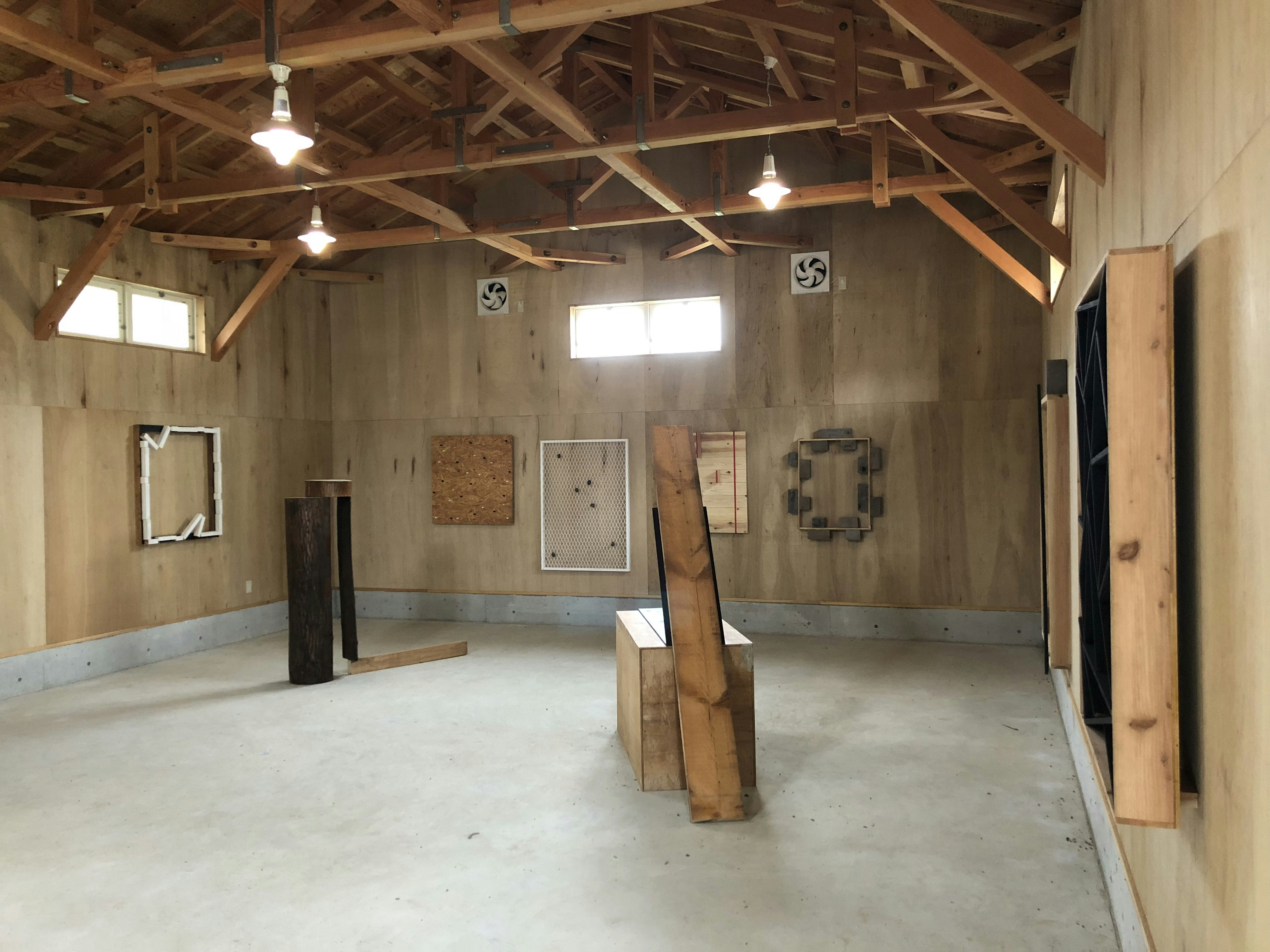 Interior of a timber studio with mounted frames on the walls and wooden structures stacked sparsely on the ground.