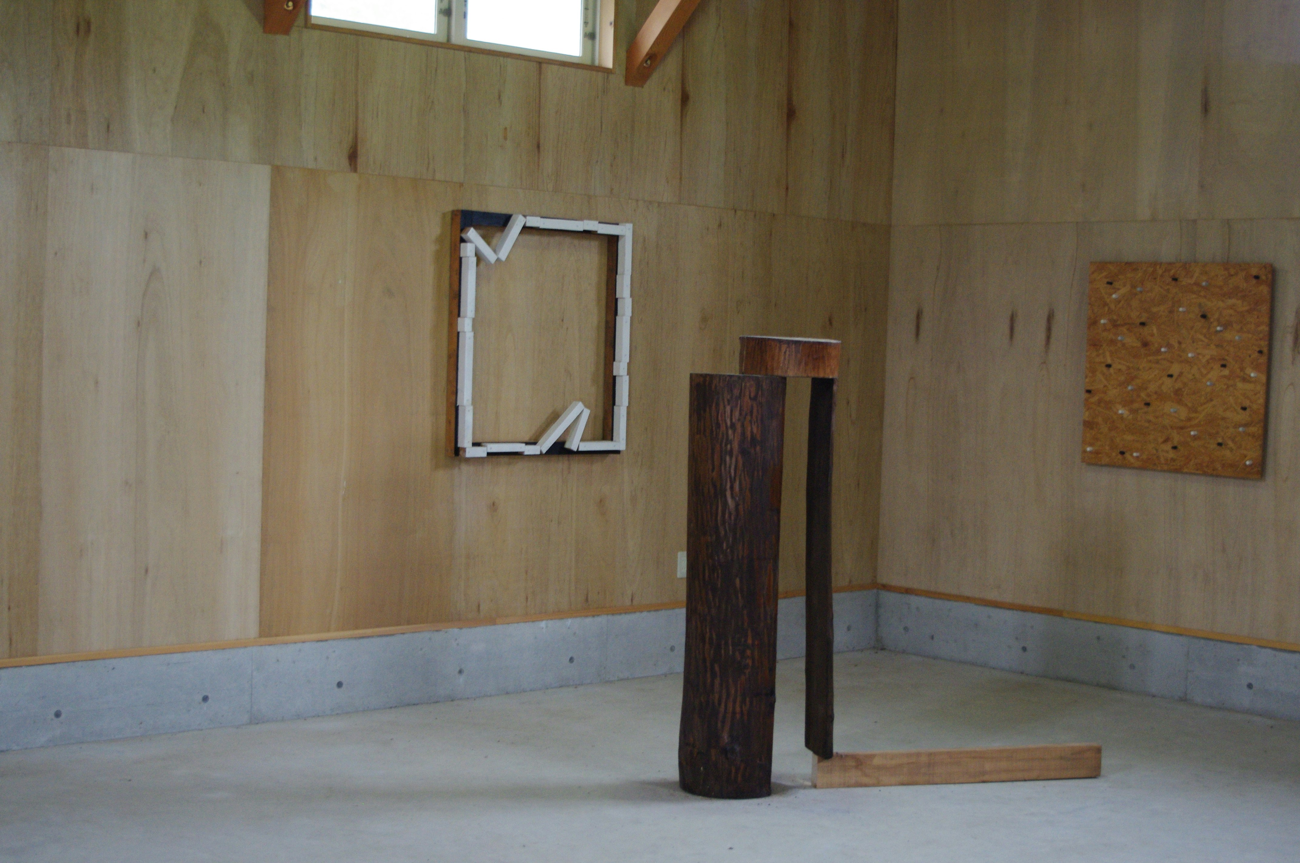 A dark timber structure built on the floor of a studio with frames mounted on the walls.