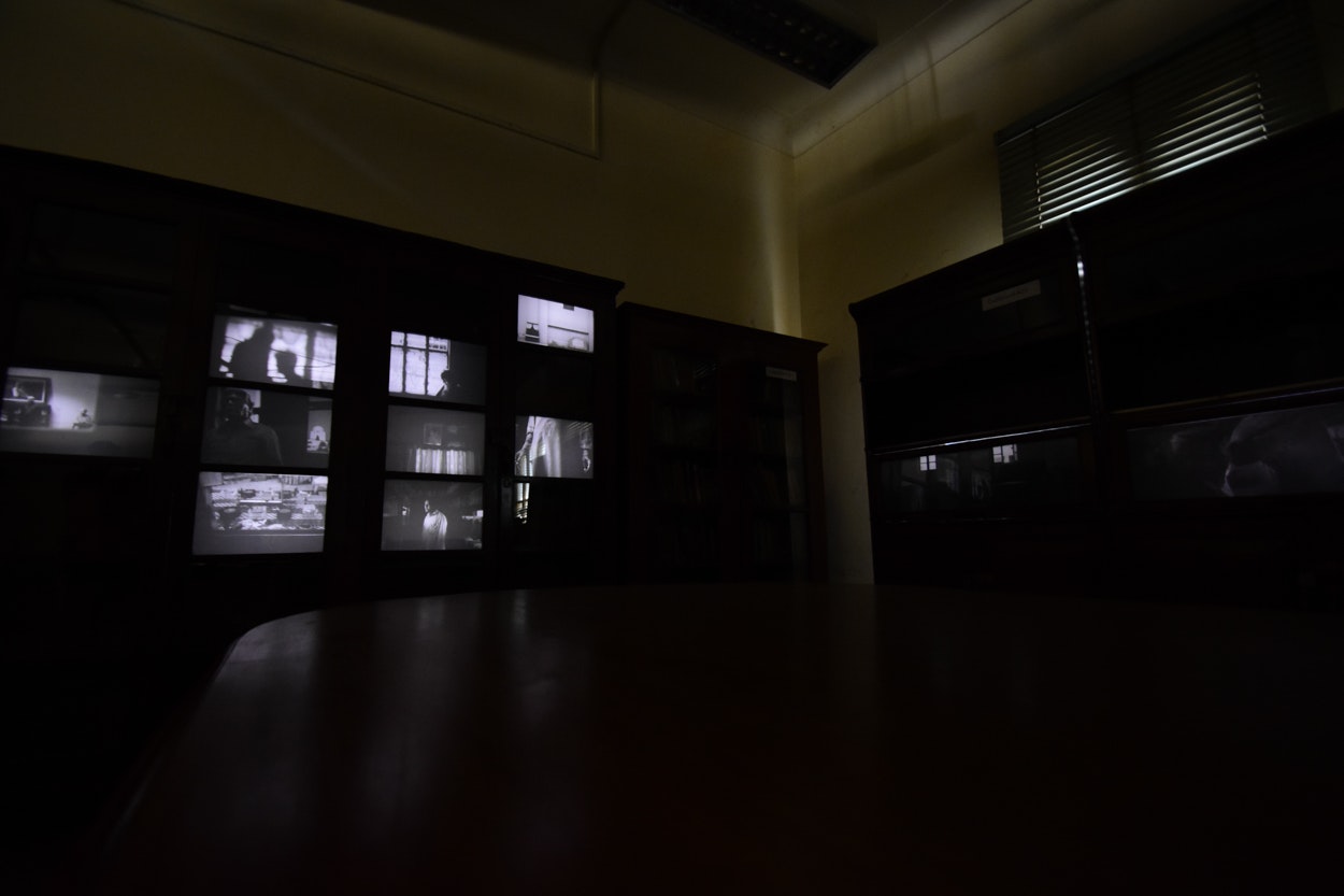 A dark room with an installation comprised of video light-boxes showing different scenes of a man walking around.