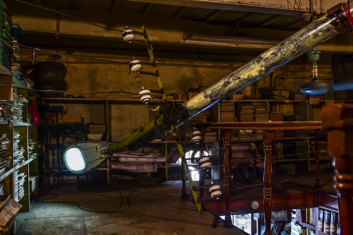 An installation of an upside-down lamppost in a room of shelves filled with old books.