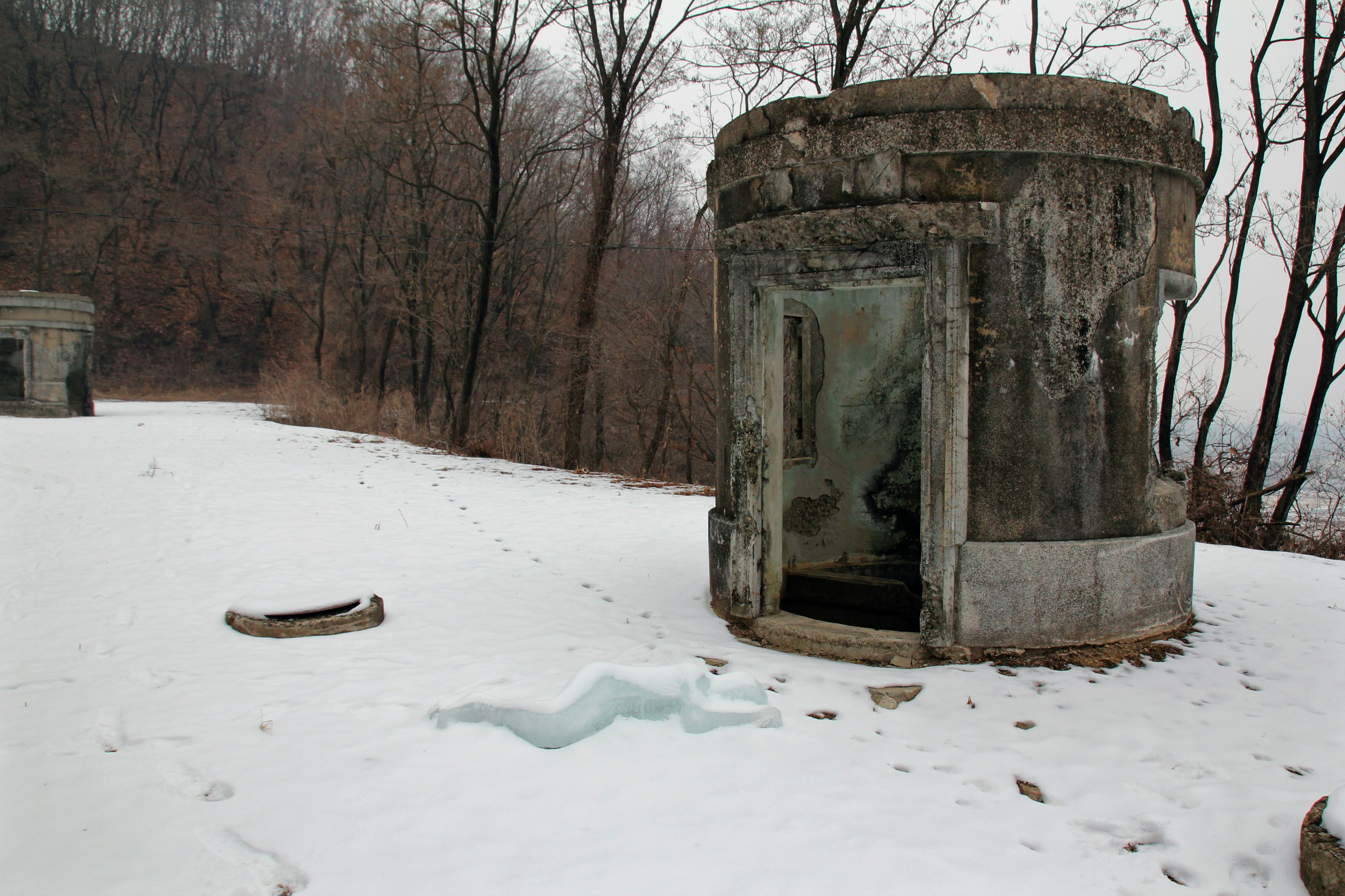 An eroded concrete structure on a path covered in snow. There are footprints leading through the snow.