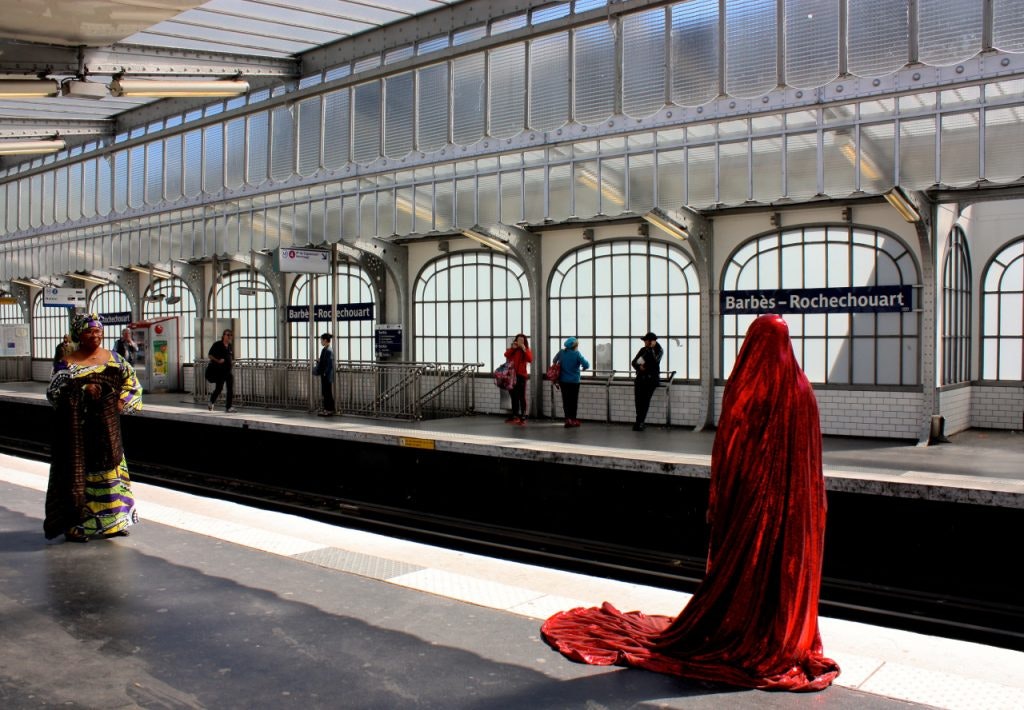 A figure in a sparkly red burqa standing on a train platform in Paris.
