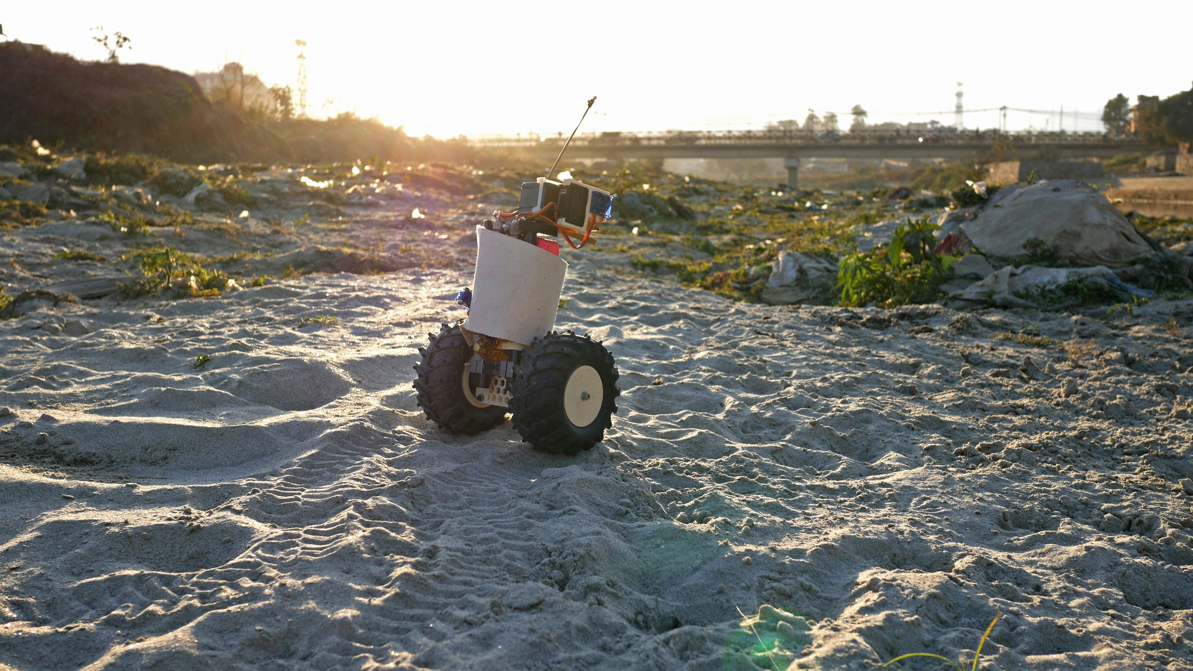 A custom-built robot rolling across sand on an urban site.