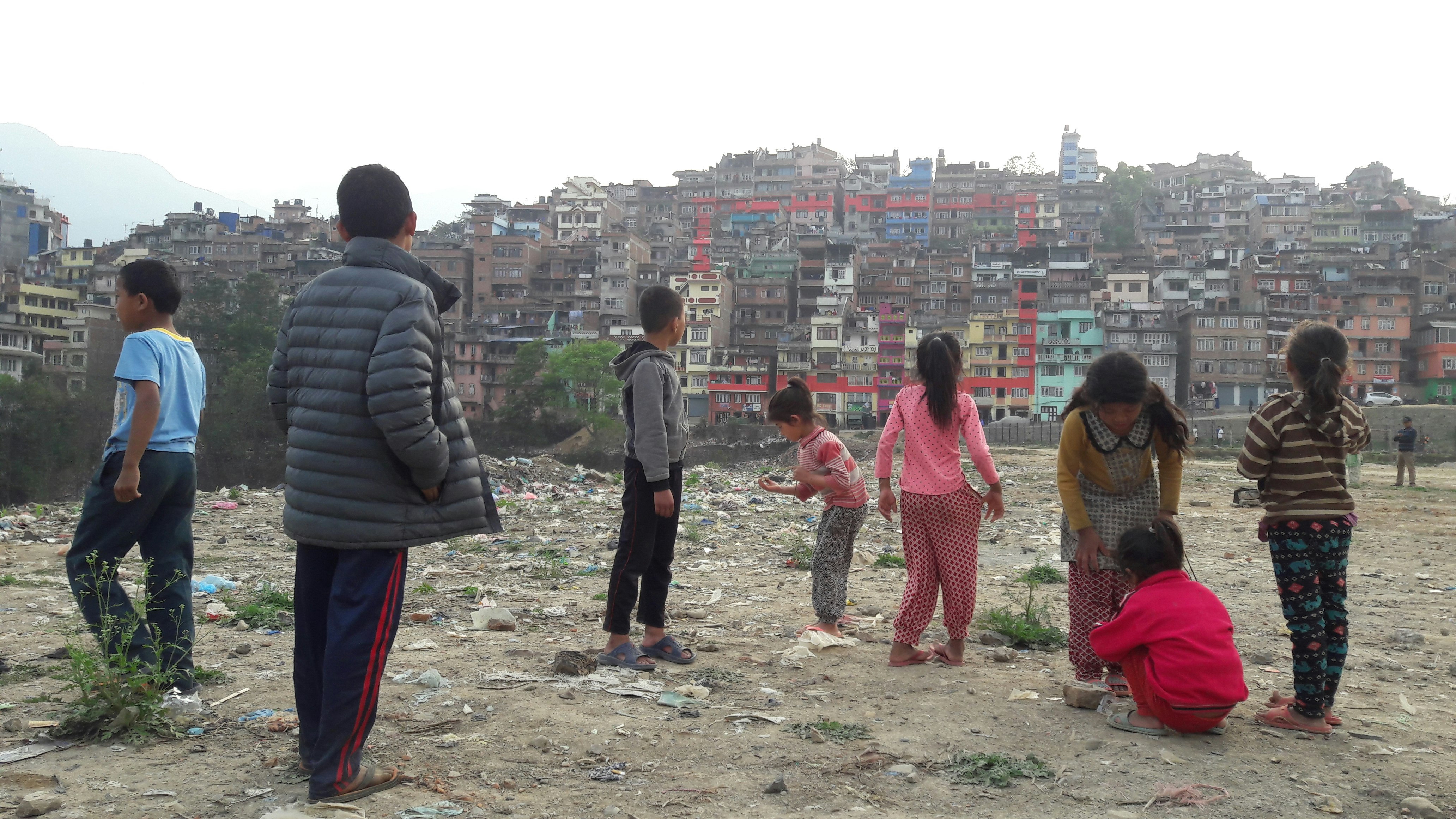 Children stand in front of a series of apartment houses in Kathmandu. A monumental rectangle is painted in red across multiple apartment facades.