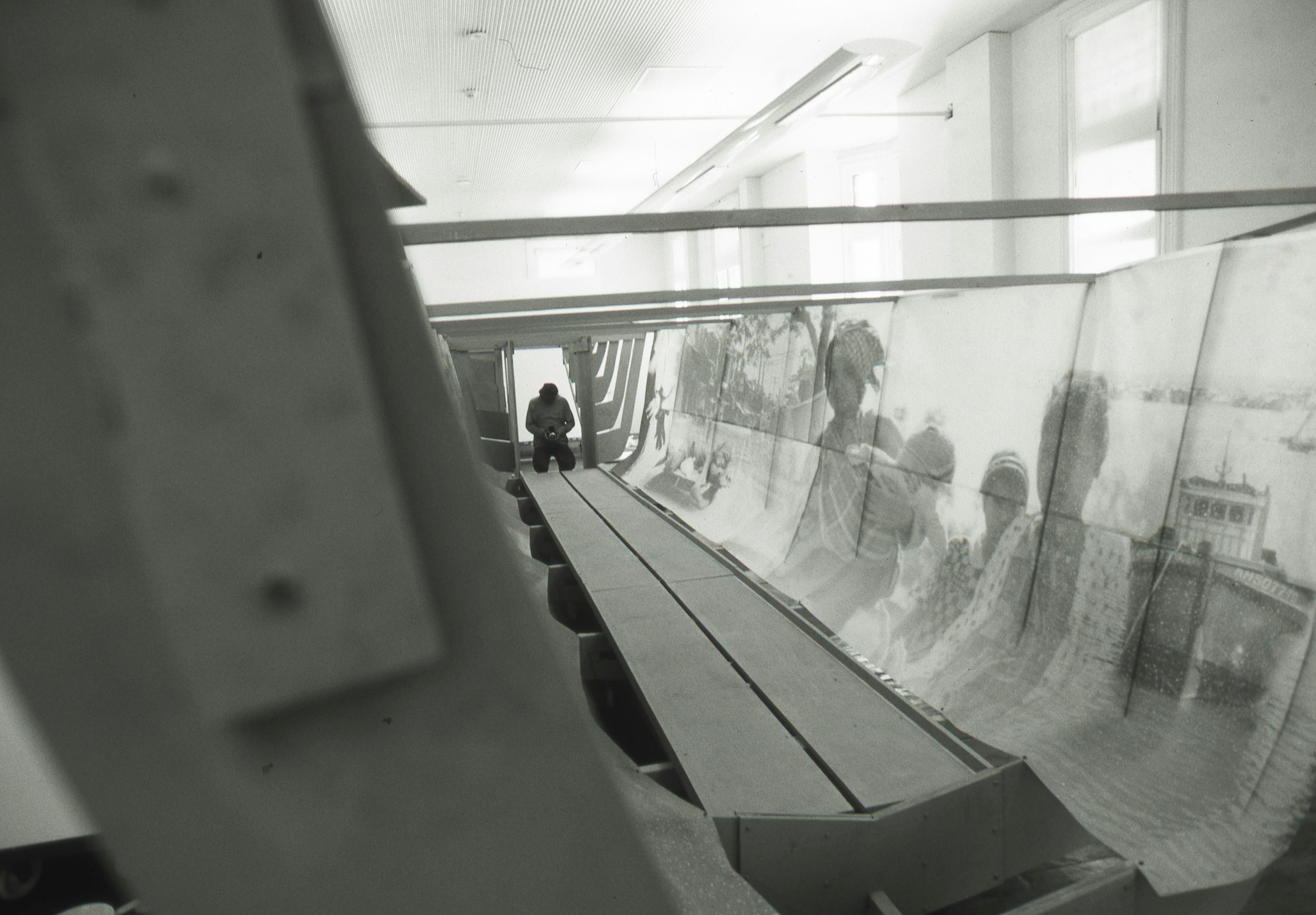 Dacchi standing on one side of a sculptural boat, holding a camera. Inside the boat are enlarged photographic prints of the Vietnamese refugee boat journey.