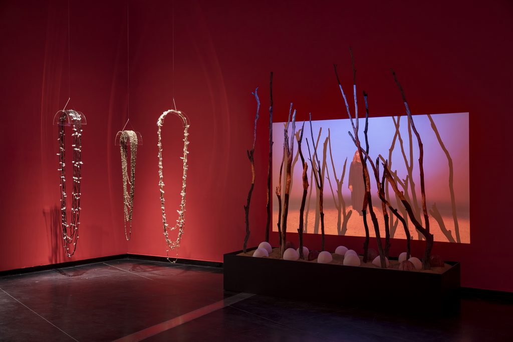 A row of branches with a projection of a woman standing in a red-lit space.