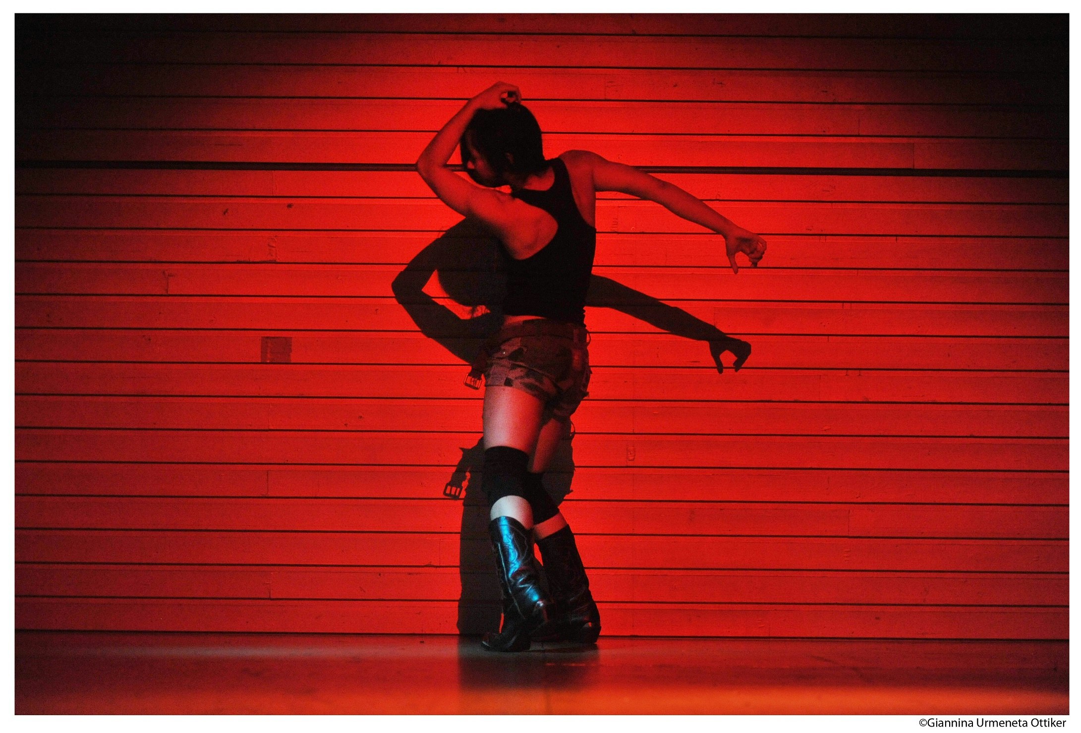 A dancer has their back to us, posing in a red spotlight.
