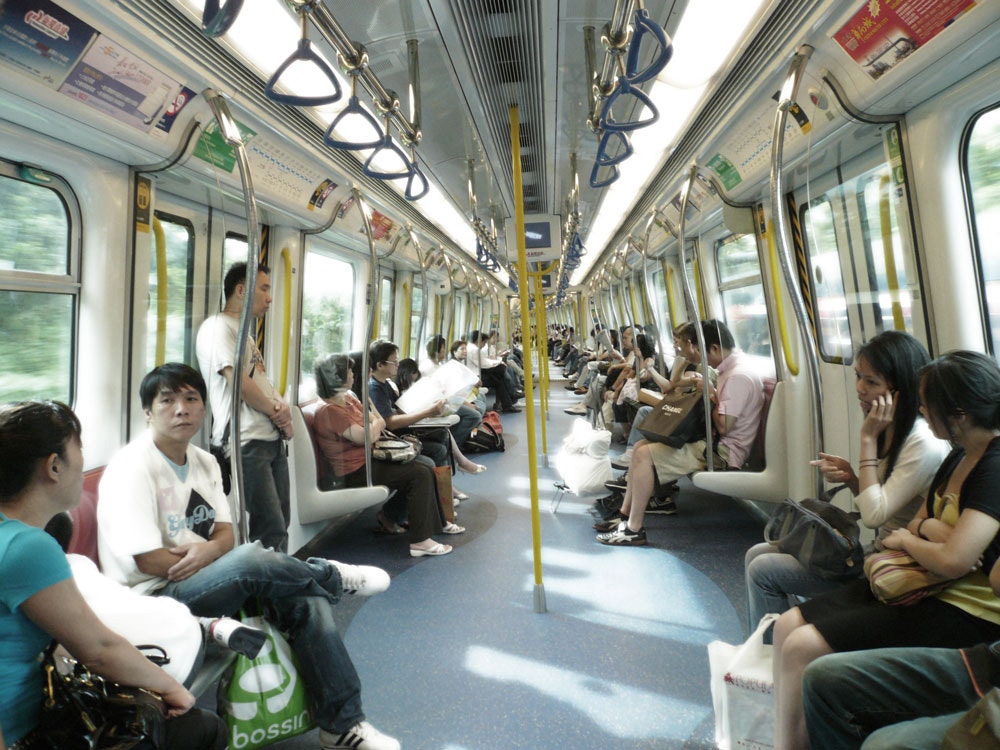 A busy MTR train in Hong Kong. Commuters are depicted on both sides of the seats.