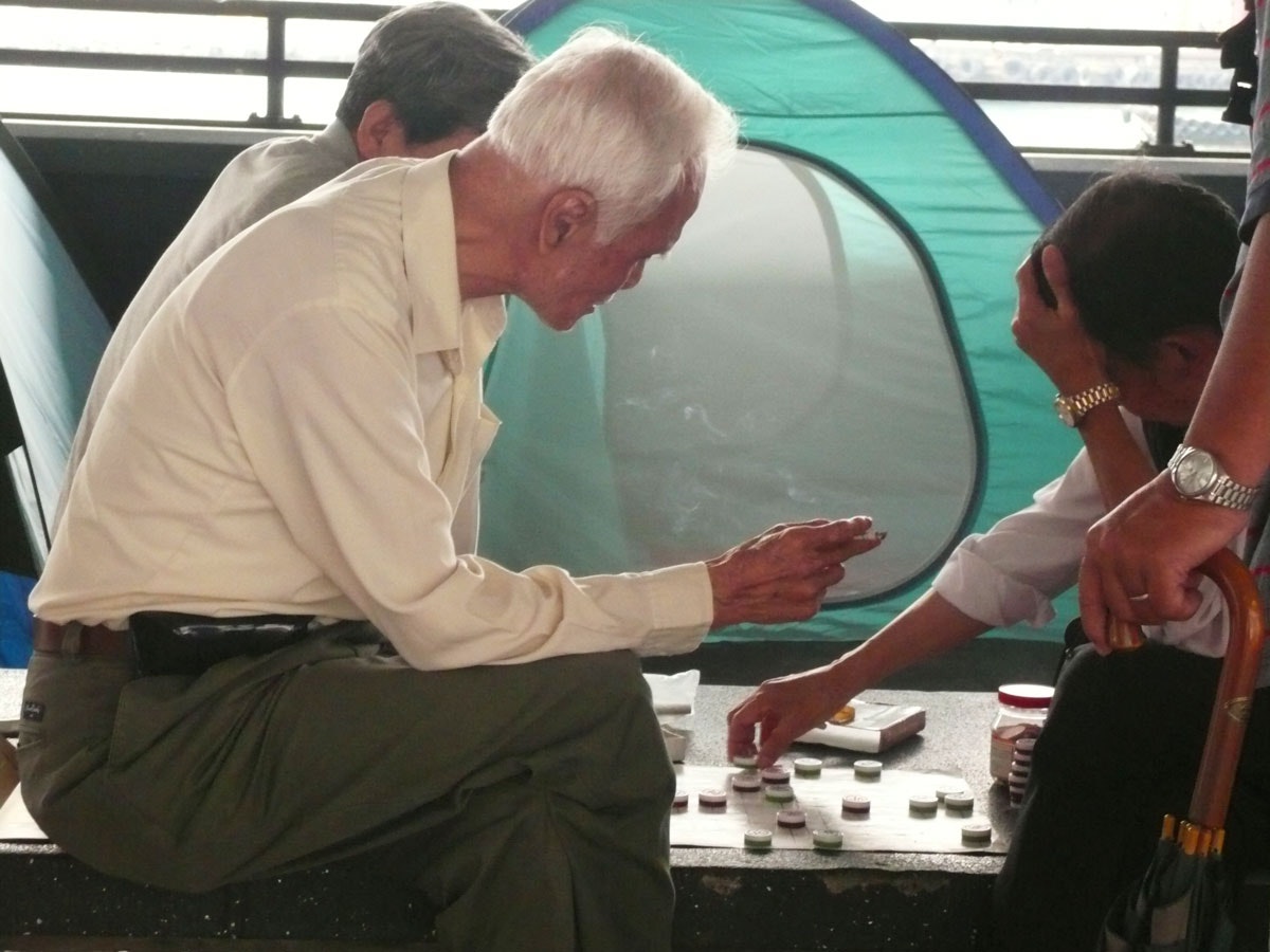 Two elderly East Asian men leaning over a gameboard.