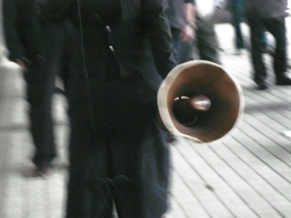 A blurred photo of a protestor wearing all black and holding a megaphone.
