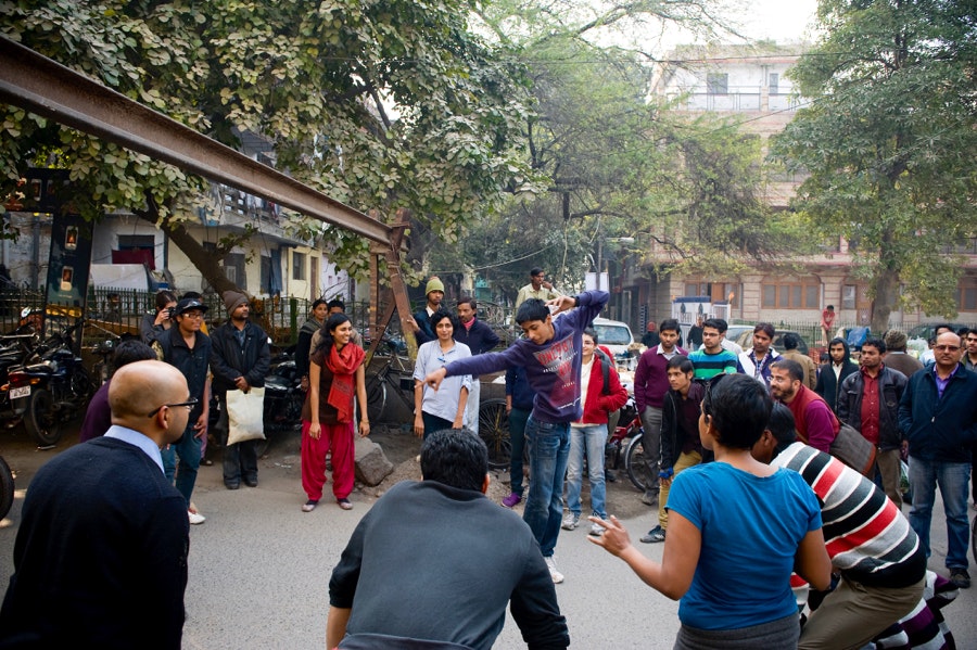 A male-presenting teenager dances in the centre of a circle of people watching him.