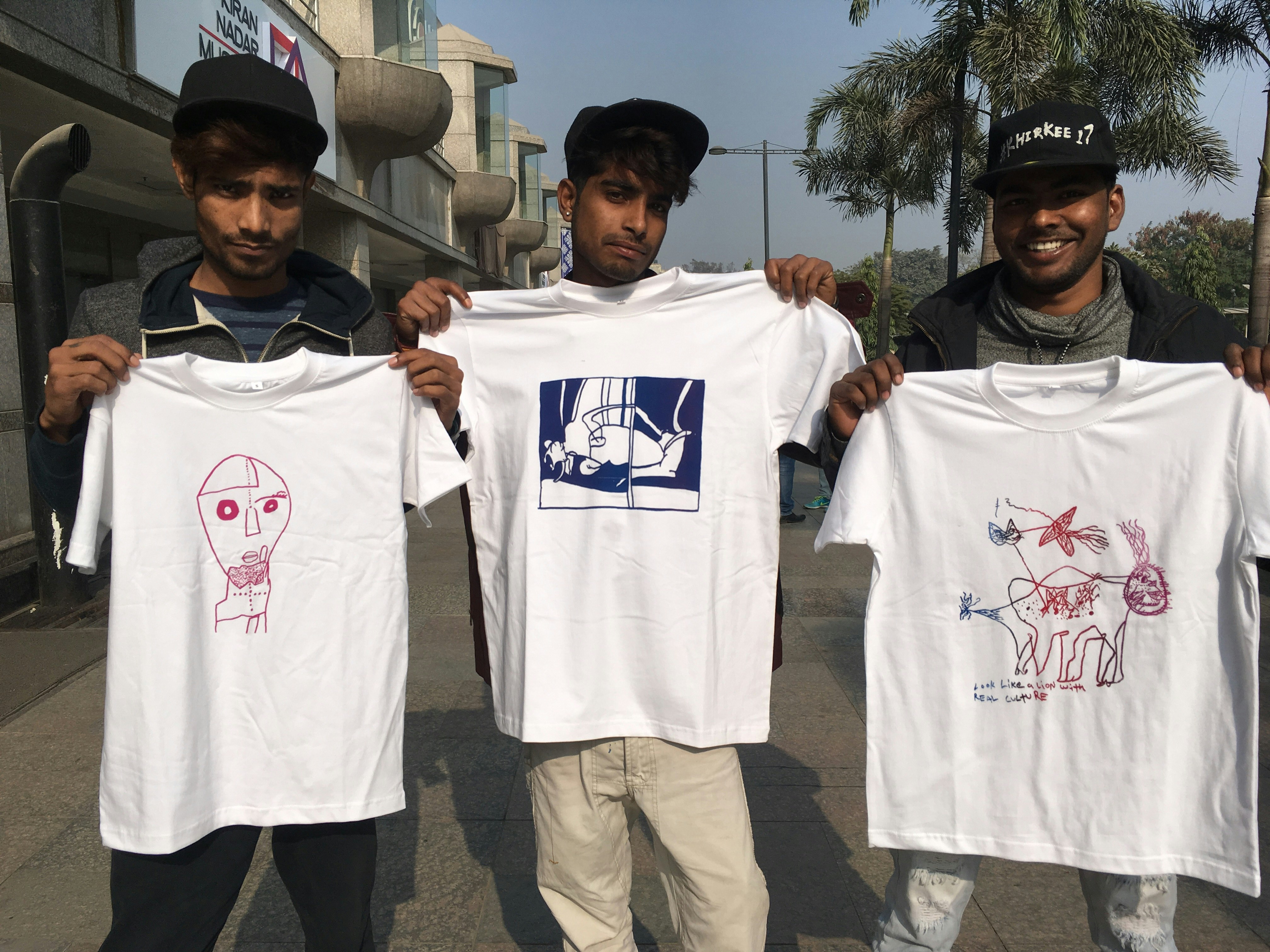 Three male-presenting figures stand holding up white screen-printed shirts.