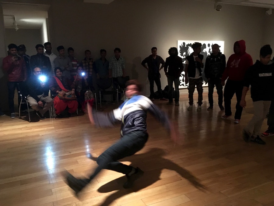 A breakdancer performs in the spotlight, in the centre of a circle of people.