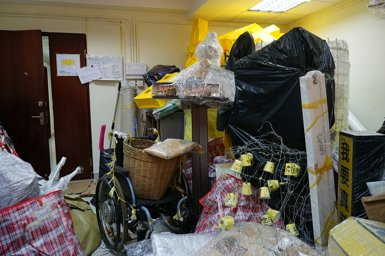 A storage space filled with plastic wrapped objects, chicken wire and and tricolour plastic bags.