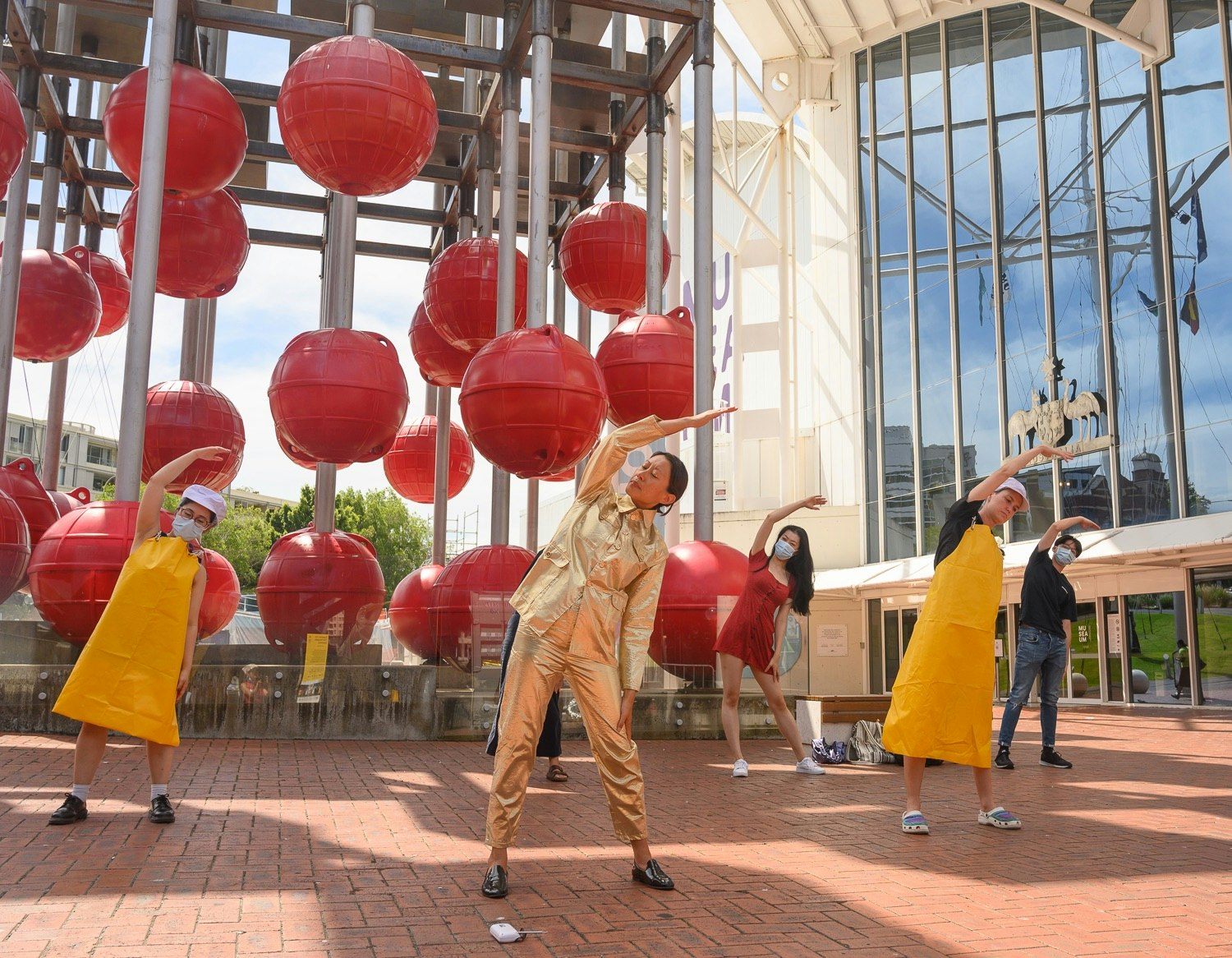 Eugenia and a group of participants dressed as factory workers do calisthenics in front of the museum.