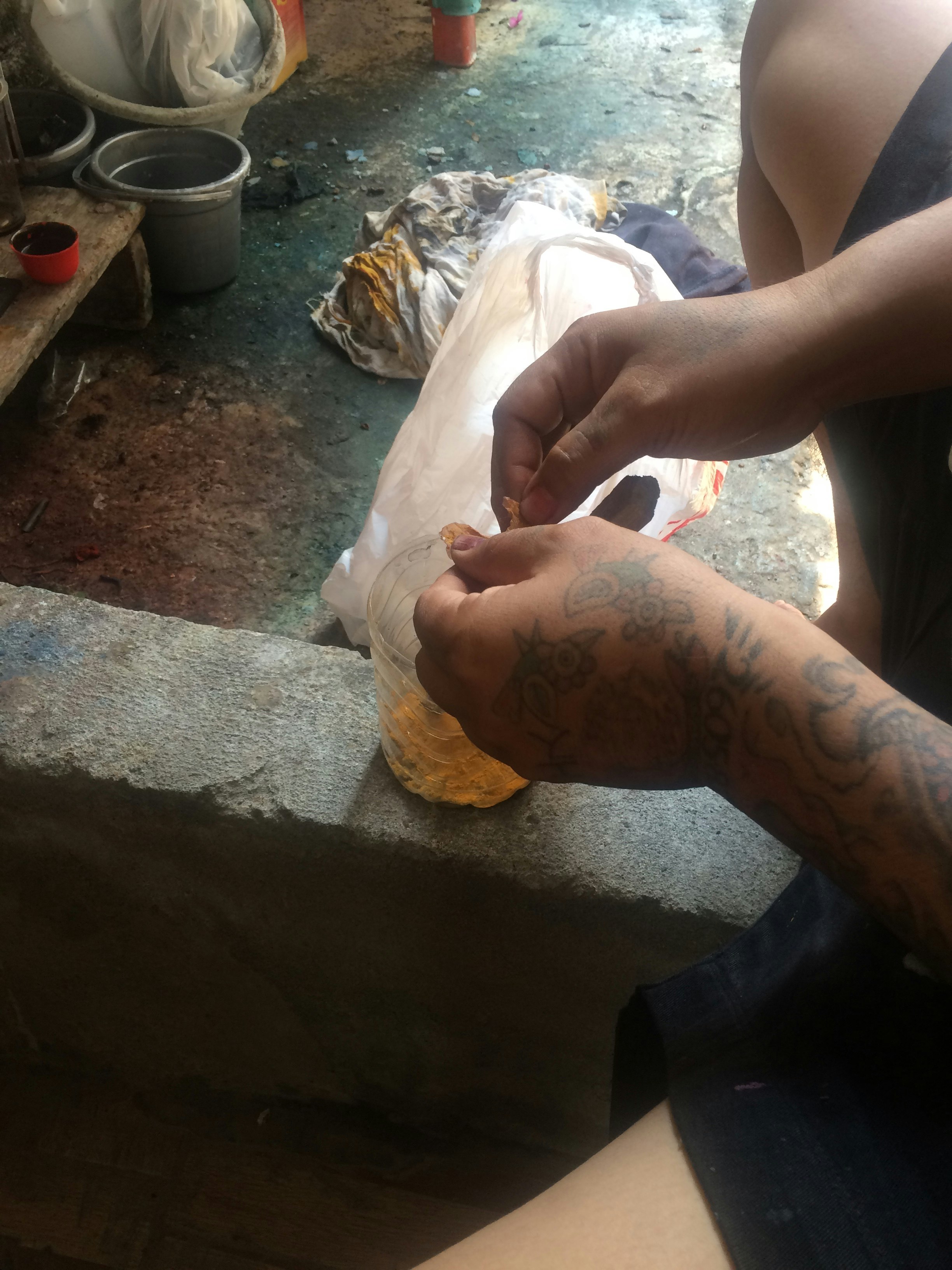 Tattooed hands tearing a chalky orange substance into a jar.