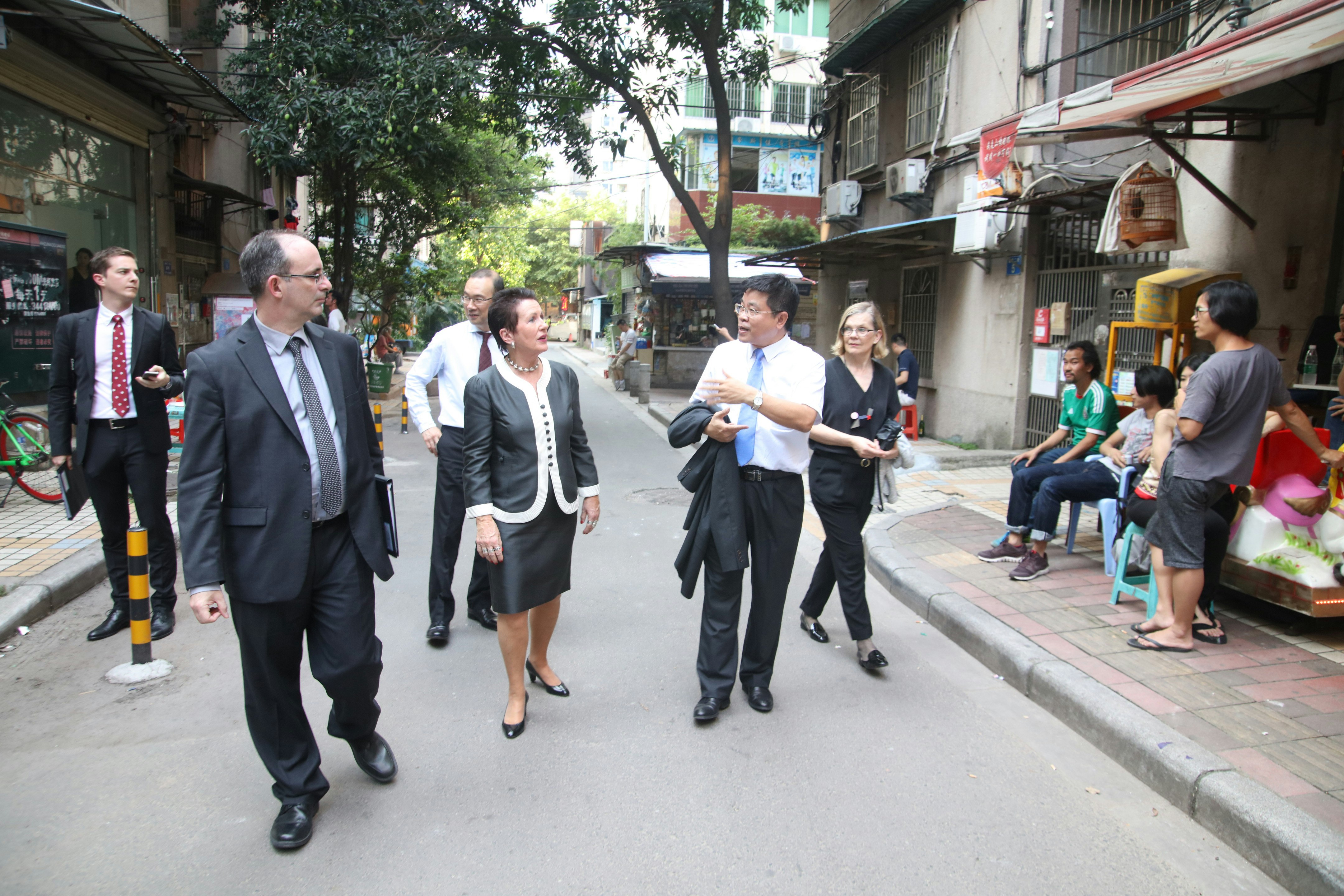 A crowd of council members dressed in business attire walk down a quiet alley.