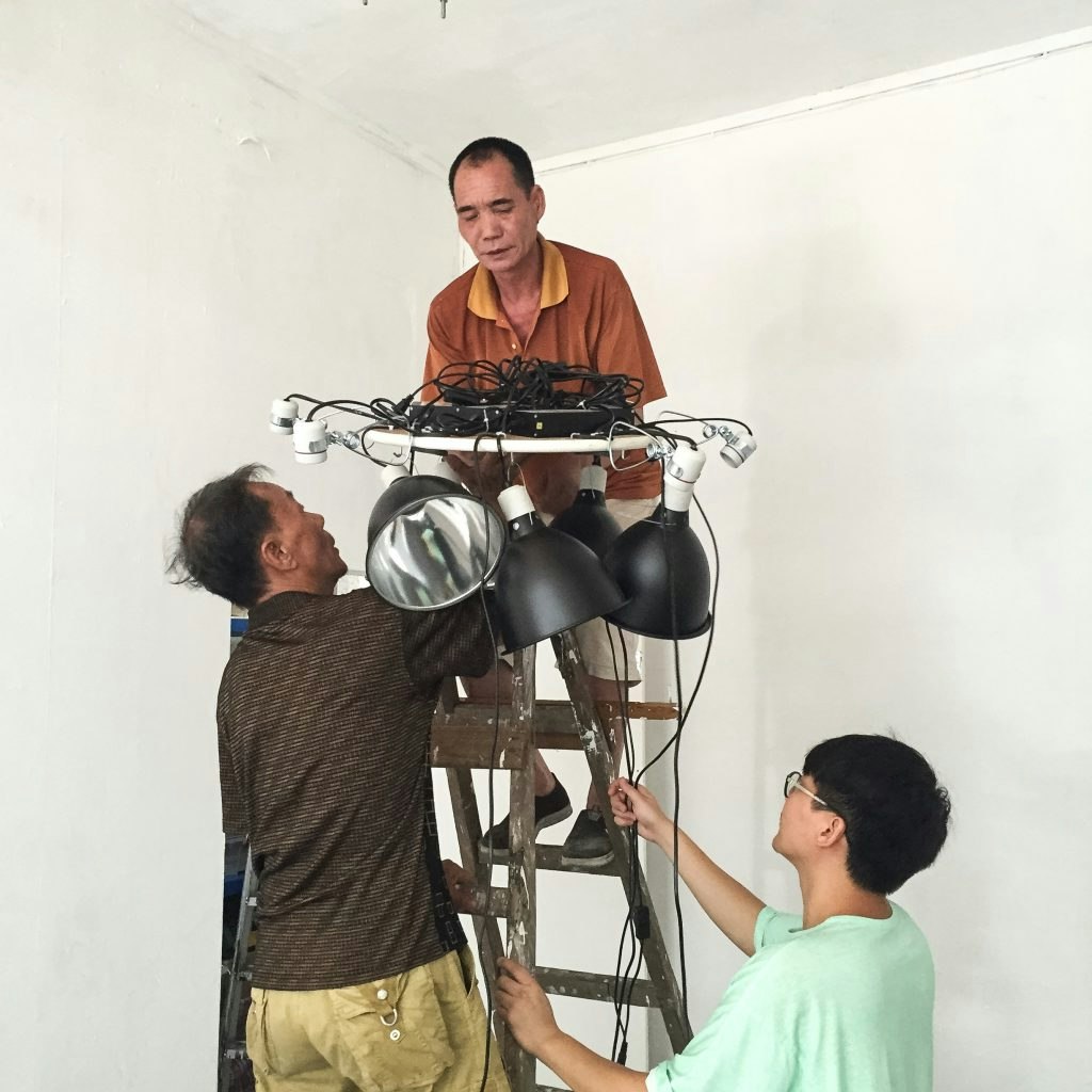Three East Asian male-presenting figures working on a lighting rig.