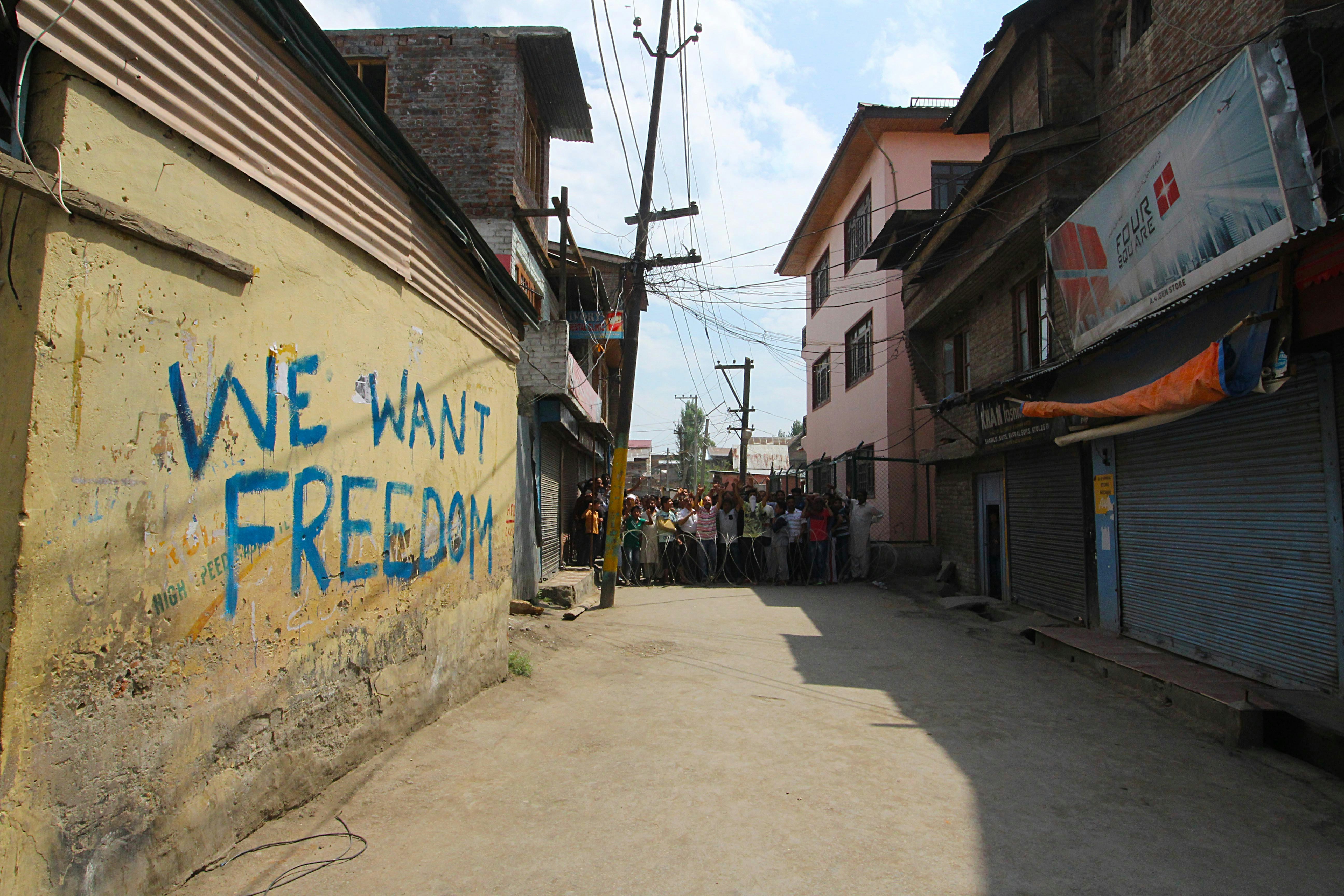 A residential street in Kashmir with the words 'We Want Freedom' grafittied on a yellow wall.