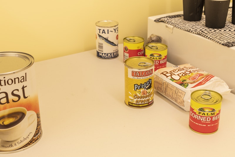 Tinned cans of corned beef, coconut cream and mackerel, a packet of breakfast crackers, a big tin of International Roast instant coffee and coffee cups on a white plastic fold-out table.