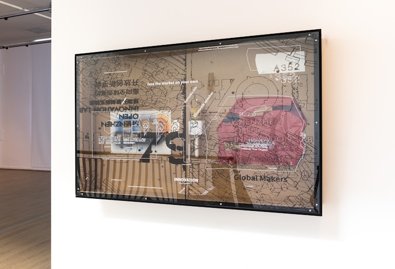 A laser-cut artwork with stencils and numbers encased is mounted on a white gallery wall