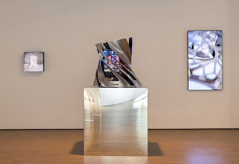 A twisted platinum sculpture with a neon-lit computer system built inside. It stands on a reflective plinth