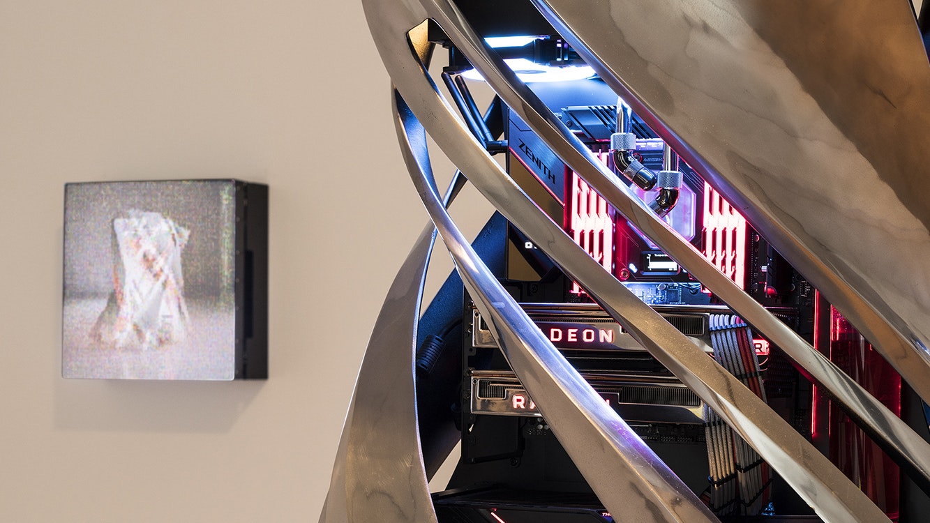 Close-up of the neon-lit computer system inside a twisted platinum metal sculpture. The computer system includes a motherboard labelled 'Zenith', installed over two graphic disks with the name 'RADEON' lit up in red on each one
