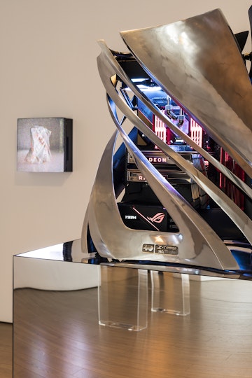 Close-up of the neon-lit computer system inside a twisted platinum metal sculpture. The computer system includes a motherboard labelled 'Zenith', installed over two graphic disks with the name 'RADEON' lit up in red on each one