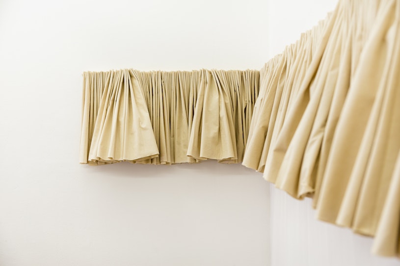A short beige fabric curtain mounted on two white gallery walls