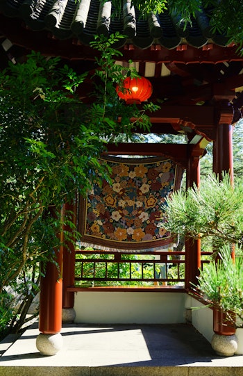 A woven tapestry of red, orange and yellow flowers, suspended in a Chinese pavilion