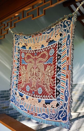 Close-up of a woven tapestry of two mirrored tigers surrounded by blue and peach-coloured clouds