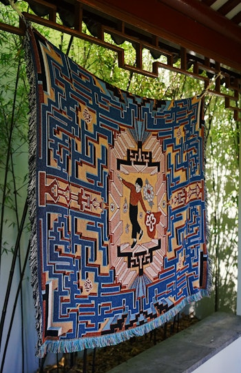 Close-up of a woven tapestry of a boy dancing in a blue maze