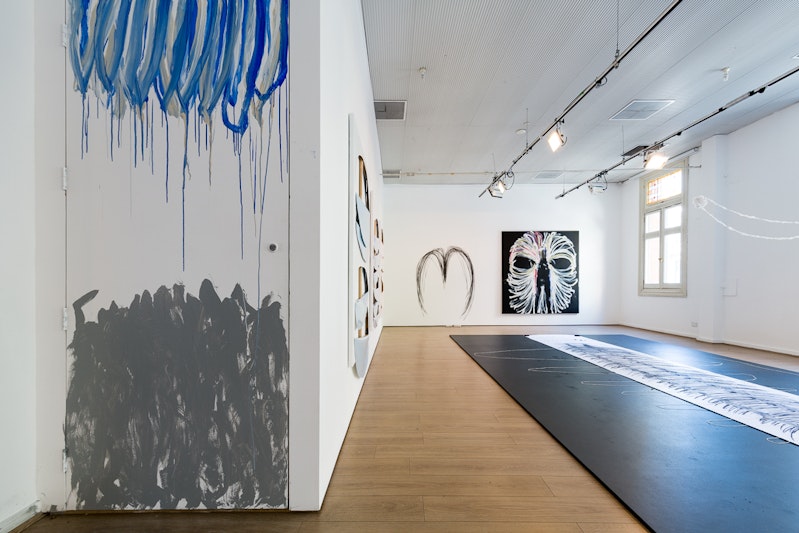 Blue and grey paint on a white gallery wall drips downwards into a mass of grey paint strokes at the bottom of the wall