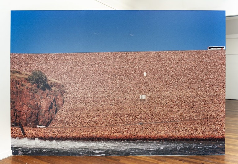 A canvas-printed photograph of a tour bus passing by a river dam surrounded by red rock.