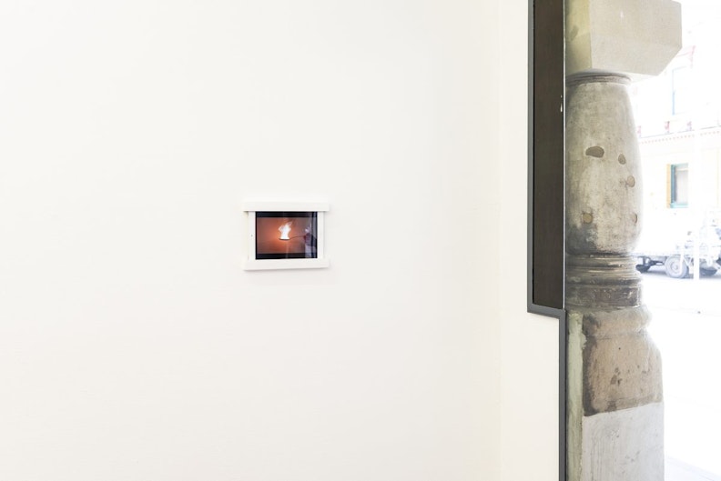 A tiny video screen in a white gallery wall, showing a spoon with burning incense.