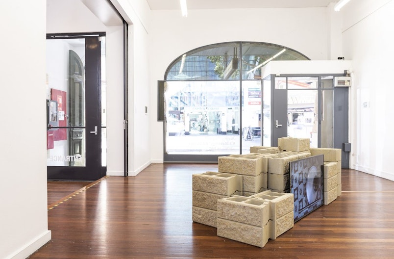 An LED video screen stood up against a mound of sandstone bricks in a light-flooded gallery space.