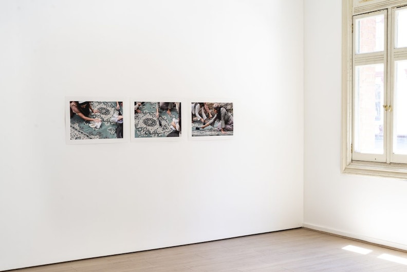 Three photographic prints showing a few femme-presenting figures dressed in muted colours with their hair tied back with bandanas, kneeling on and scrubbing a teal green Persian rug.