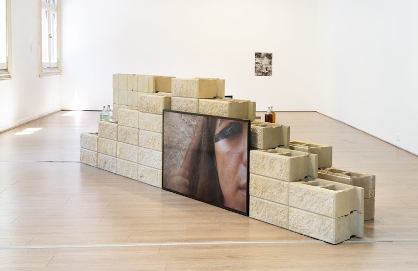 A wall constructed from sandstone brick with a LED video screen showing a close-up of one half of a face with black kohl painted over a closed eyelid.