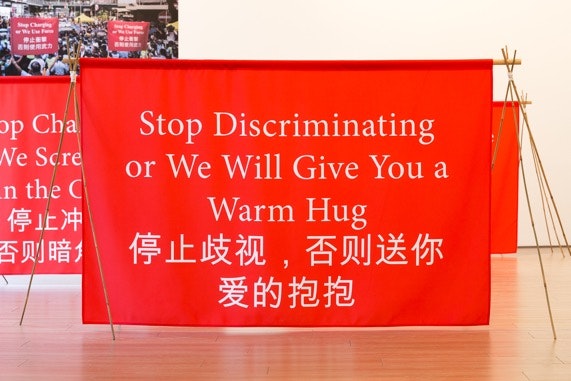 A banner made of red cloth were placed on the ground, with the words "Stop Discriminating or We Will Give You a Warm Hug" written in English and Chinese.