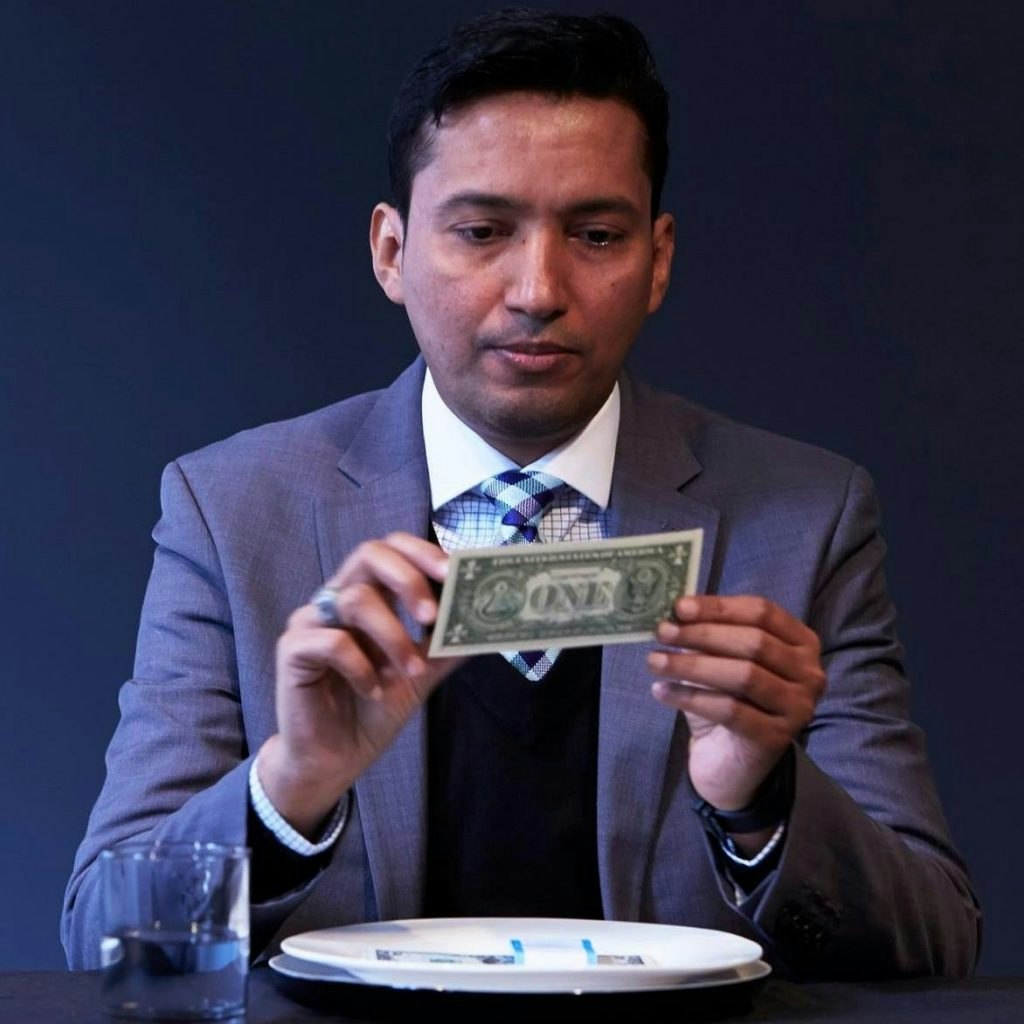 A man in a suit holds a One dollar bill with both of his hands. He stares at it intendly.