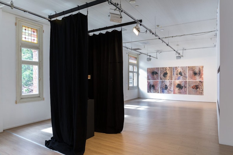 Black curtains drape down from the centre of the gallery, and copper-etched artworks displayed on the wall at the back