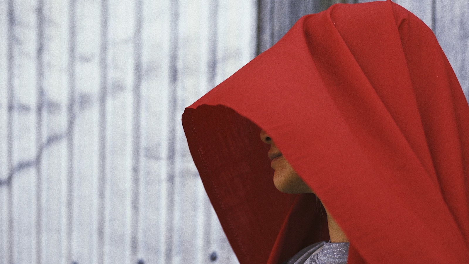 Red fabric hooded over performer’s left-sided face profile; minimal parts of neck, chin, lips and nose delicately exposed